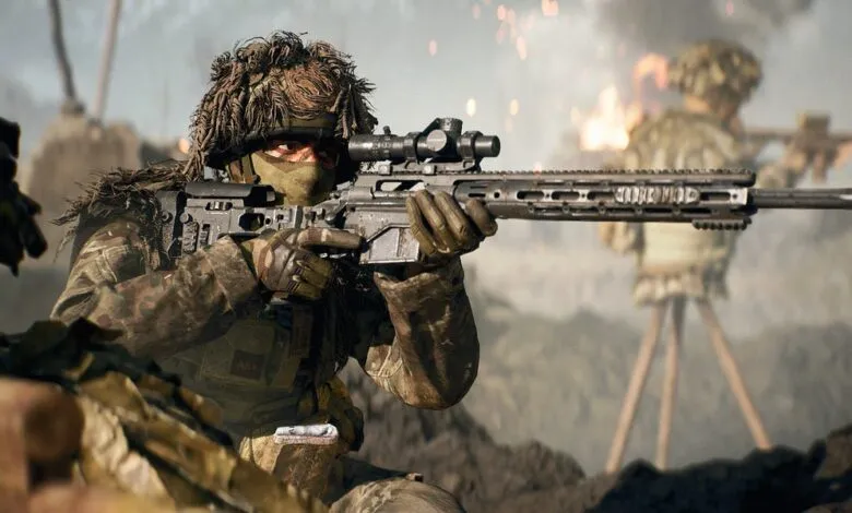 Soldier in camouflage aiming a sniper rifle with a scope, with another soldier in the background.