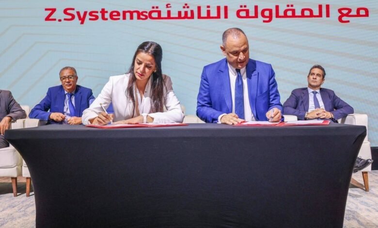 Business professionals signing a contract at a table with Z.Systems logo in the background.