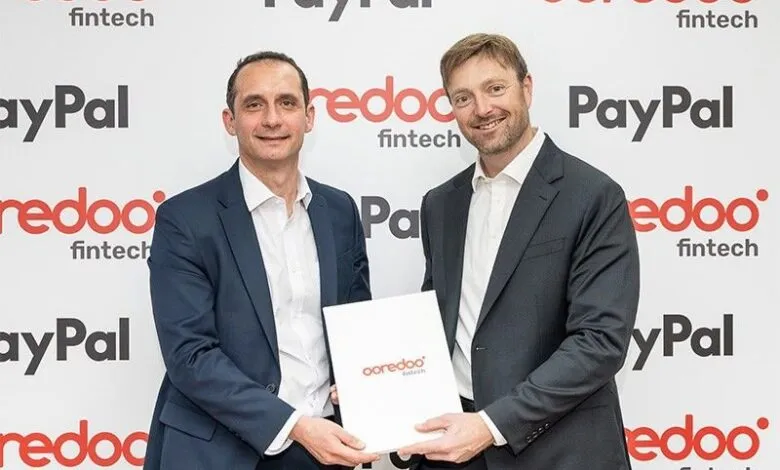 Two men in suits hold a document with Ooredoo Fintech logo, with Ooredoo Fintech and PayPal logos in the background.
