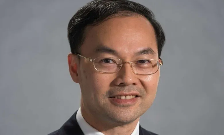 Close-up portrait of an Asian man wearing glasses and a dark suit.