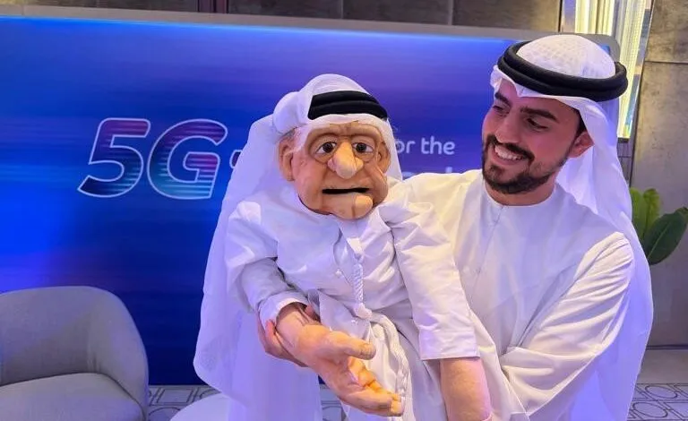 Man in traditional Emirati clothing holding a puppet with a large nose and white attire.