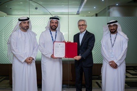 Four men in formal attire, three in traditional Emirati dress, pose for a photo during a document signing.