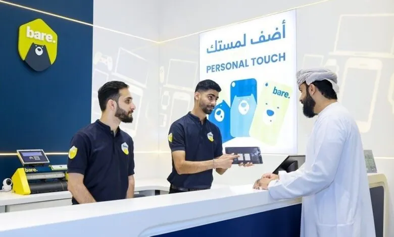 Two store employees assist a customer at a counter in a brightly lit retail store.