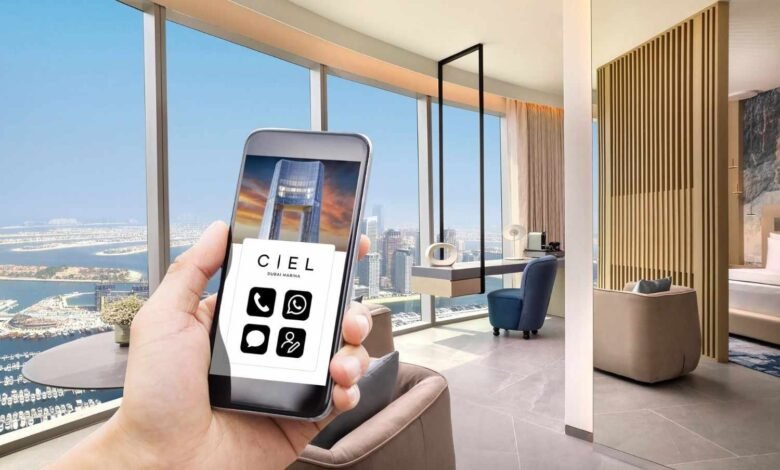 Hand holding a smartphone displaying Ciel Dubai Marina contact icons with a luxury hotel room view.