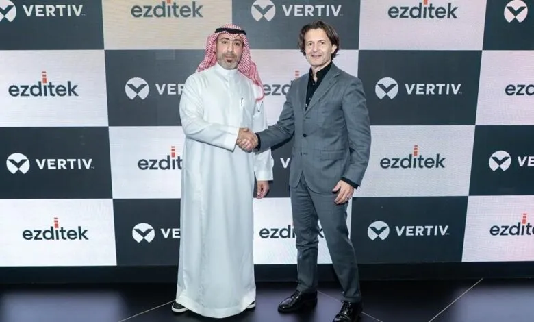 Two men in business attire shaking hands in front of a branded backdrop.