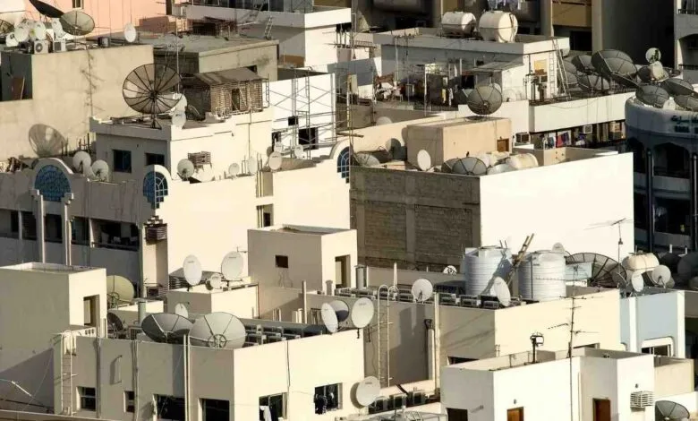 Rooftops densely packed with satellite dishes and water tanks in an urban environment.