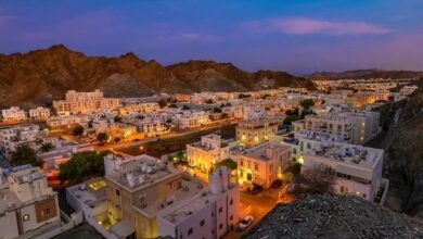 Aerial view of a city nestled against rugged mountains at dusk, with illuminated buildings.