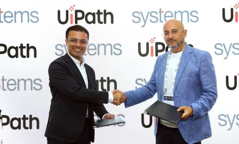 Two men in business attire shaking hands in front of a UiPath Systems backdrop.