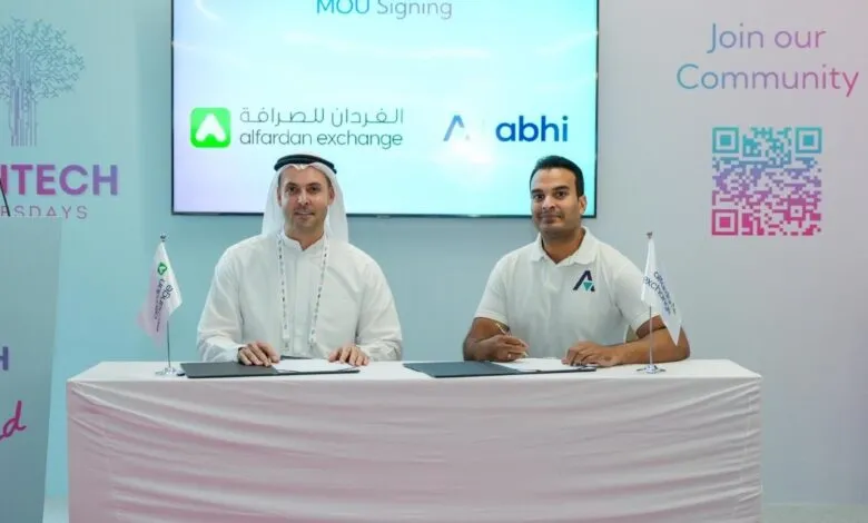 Two men signing an MOU, with company logos displayed on a screen and flags on the table.