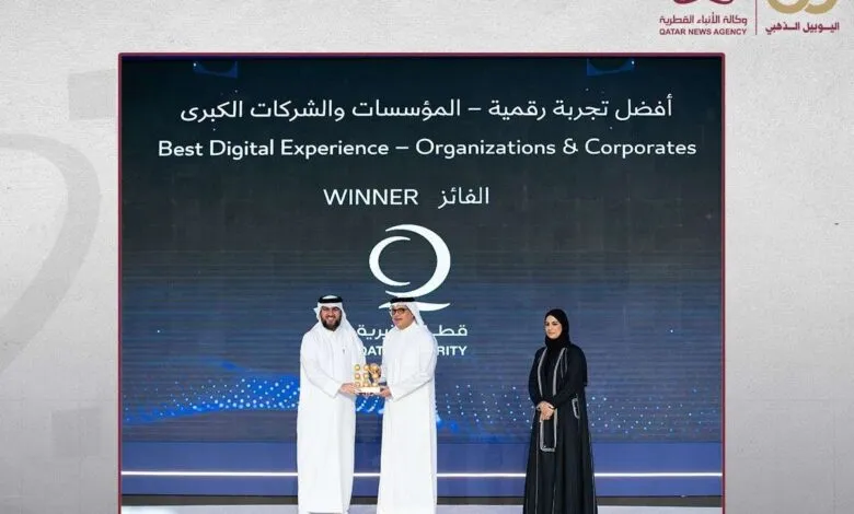 Two men in white thobes receive an award on stage, with a woman in a black abaya standing nearby.