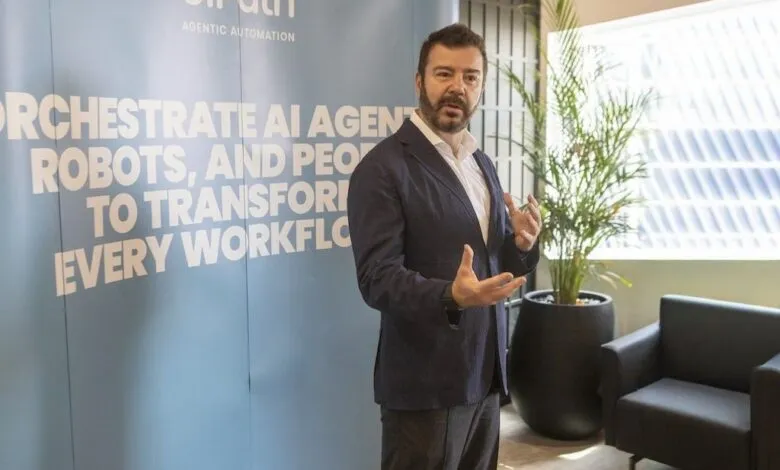 Man in a suit speaking in front of a UiPath banner about automating workflows.