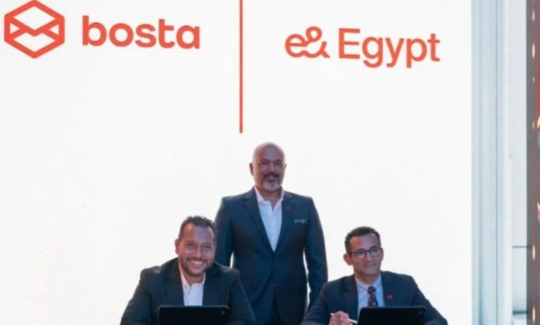 Three men in suits posing in front of Bosta and e& Egypt logos.