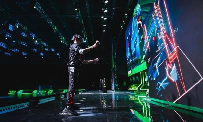 Person wearing VR headset and holding controllers, playing a game on a large screen.