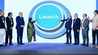 A diverse group of professionals stand on stage, gesturing towards a large circular screen displaying the word 'Launch'.