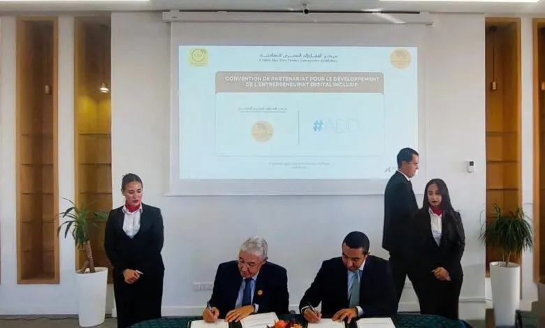 Two men in suits sign documents at a table, with two formally dressed women standing behind them.