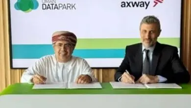 Two men signing a document at a table, with company logos in the background.