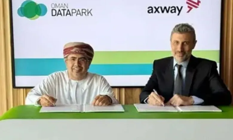 Two men signing a document at a table, with company logos in the background.