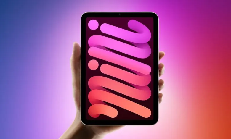 A hand holds an iPad Mini displaying a colorful, abstract wallpaper with pink and orange swirls.