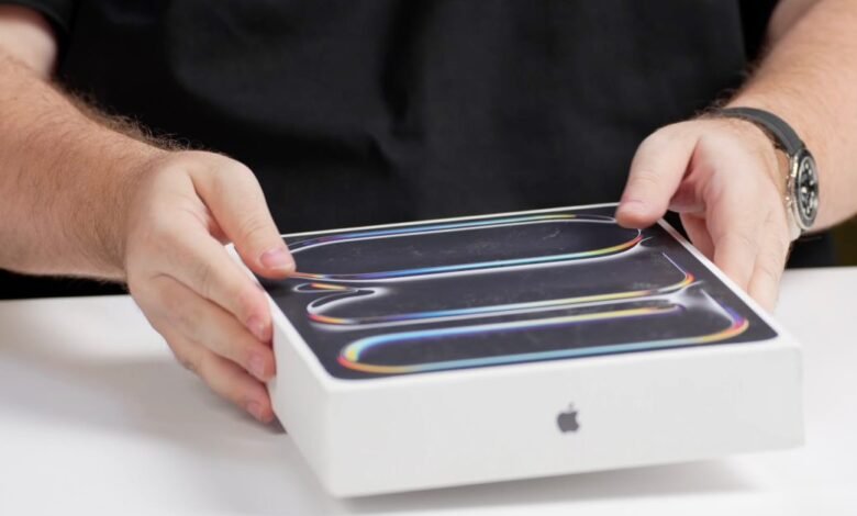 Hands holding a white Apple product box with a colorful, abstract design on the lid.