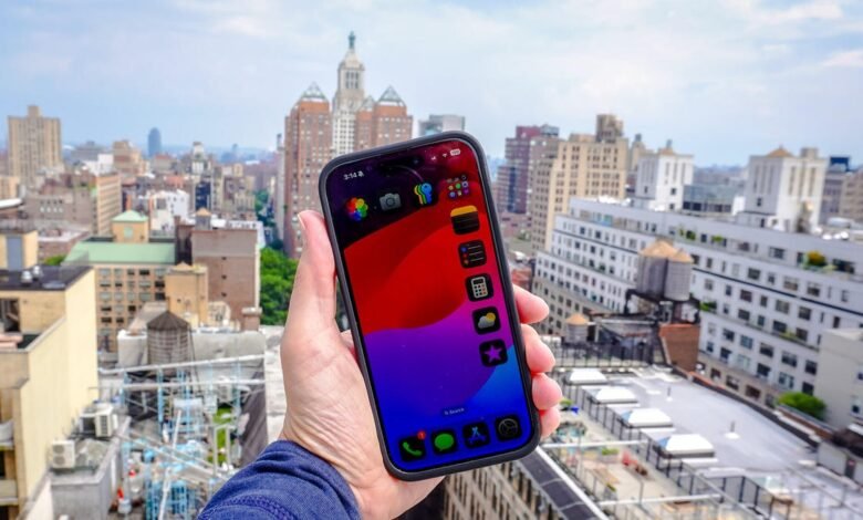 Hand holding an iPhone displaying a colorful abstract wallpaper and app icons against a cityscape.