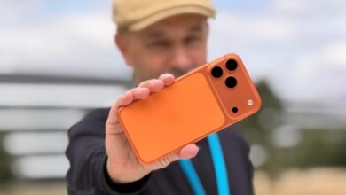 Man holding an orange iPhone with a triple-lens camera system.
