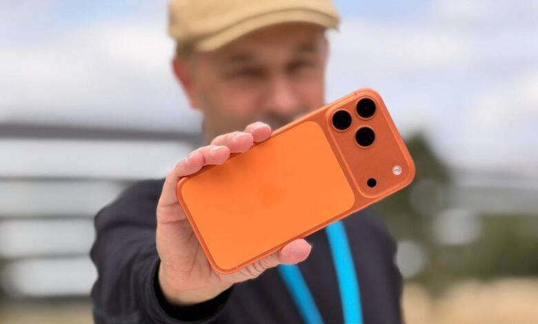 Man holding an orange iPhone with a triple-lens camera system.