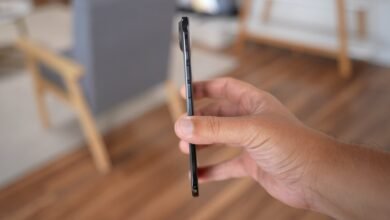 Close-up of a hand holding a thin, dark smartphone, showing its side profile and buttons.