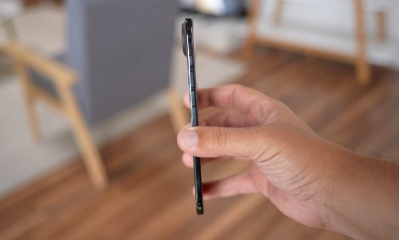 Close-up of a hand holding a thin, dark smartphone, showing its side profile and buttons.