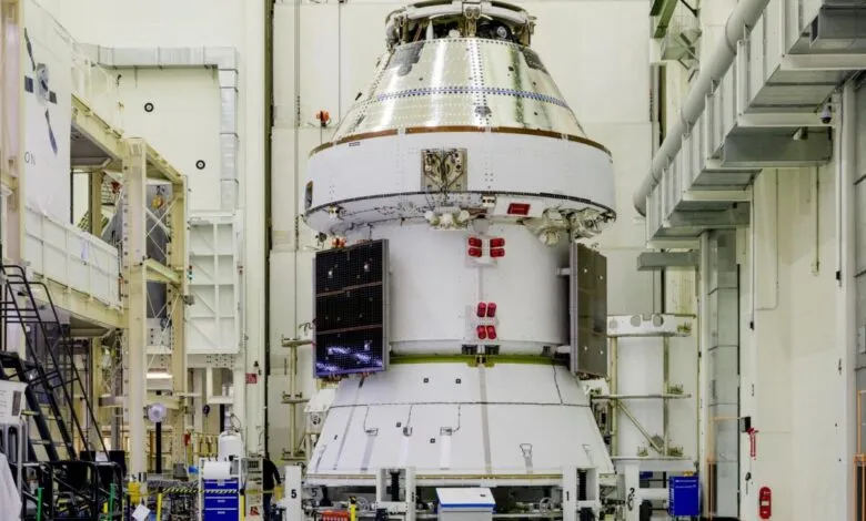 A large, white spacecraft module with solar panels attached, in a clean industrial facility.