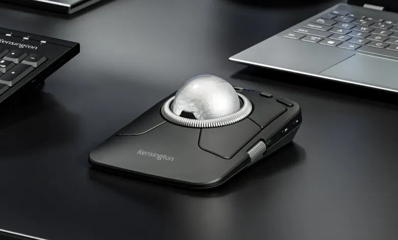 Close-up of a black Kensington trackball mouse with a silver ball on a dark desk.