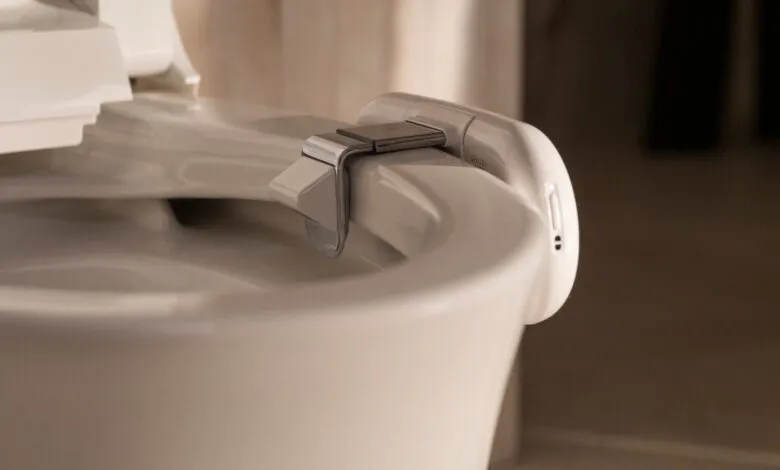 Close-up of a modern bidet attachment with a sensor on a white toilet seat.