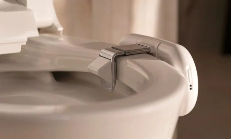 Close-up of a modern bidet attachment on a white toilet seat.
