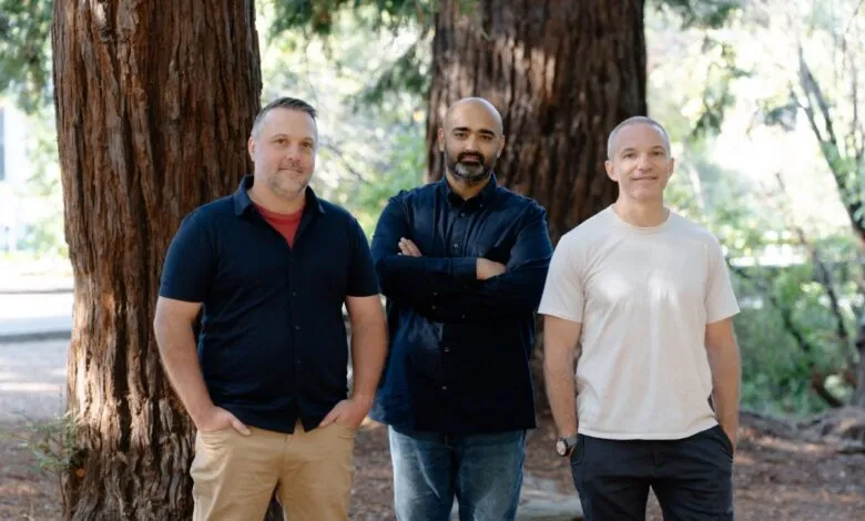 Three men standing outdoors in front of large trees, posing for a photo.