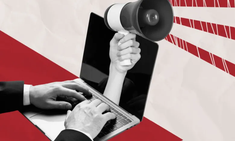 Hand typing on laptop as another hand emerges from screen holding a megaphone.