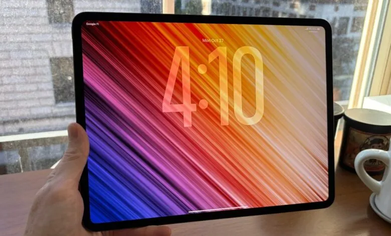A hand holds a modern tablet displaying a colorful abstract wallpaper with the time 4:10.