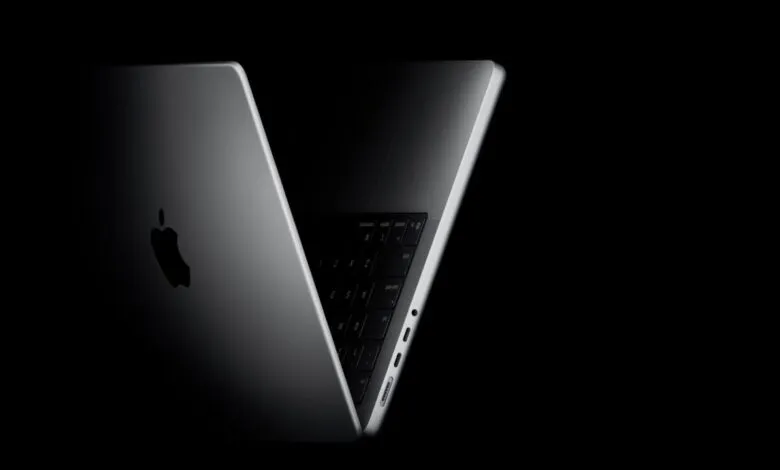 Close-up of a silver MacBook Pro with the Apple logo illuminated against a dark background.