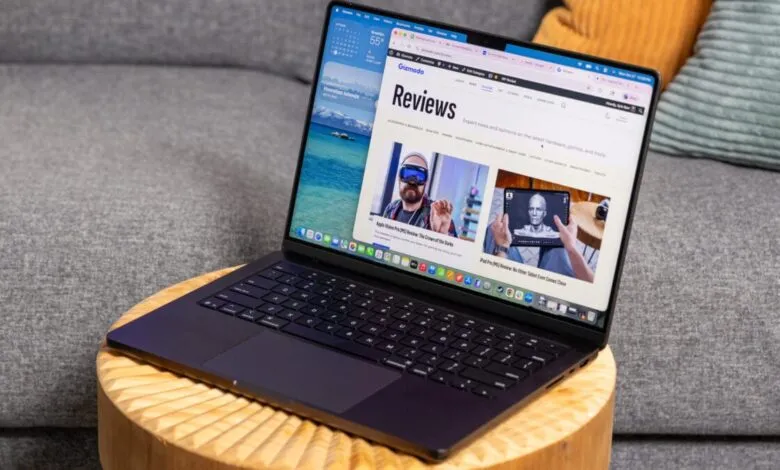 A dark MacBook Pro laptop open on a wooden table, displaying a Gizmodo reviews page.