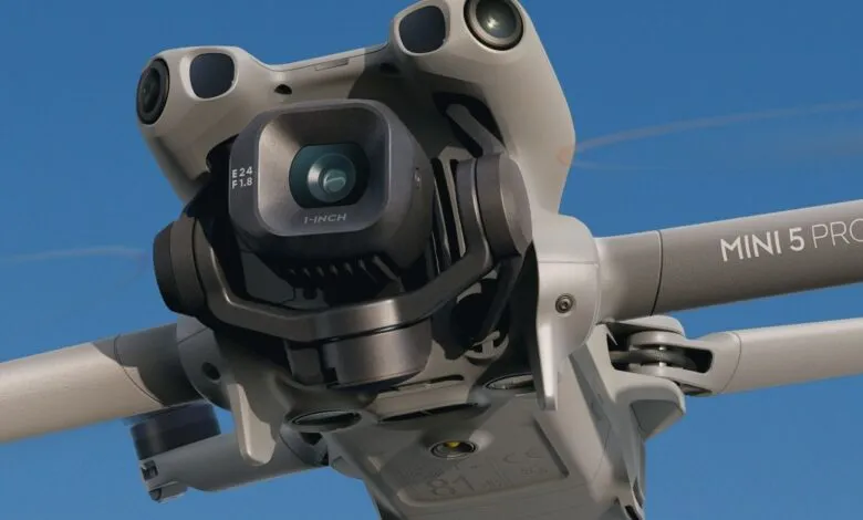 Close-up of a DJI Mini 5 Pro drone with its camera gimbal and propellers against a blue sky.
