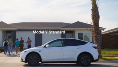 A white Tesla Model Y parked in front of a suburban house with a family walking towards it.