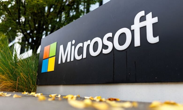 Microsoft logo sign with colorful squares and white text, outdoors with greenery and fallen leaves.