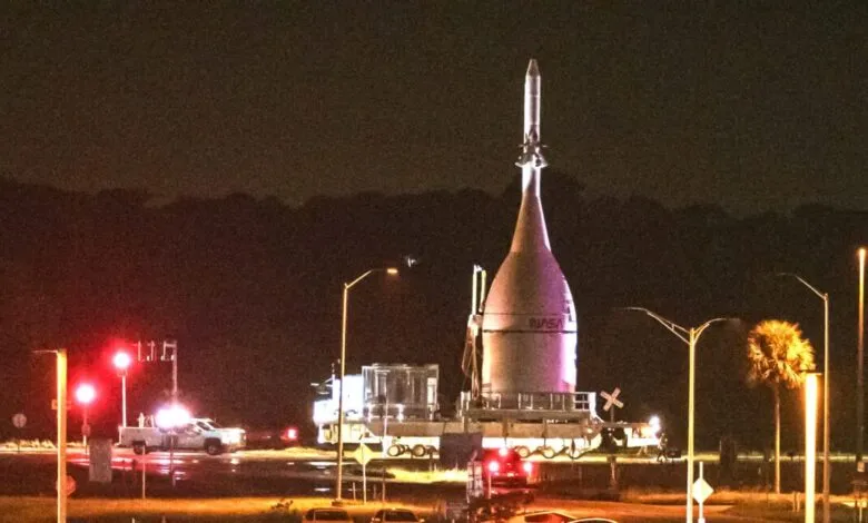 NASA rocket on transport crawler at night, illuminated by lights.