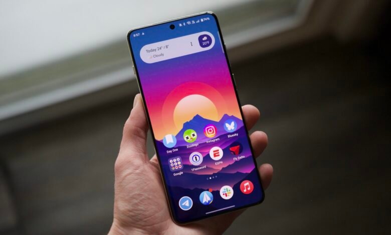 A person holds a smartphone displaying the OxygenOS 15 home screen with a vibrant mountain sunset wallpaper.