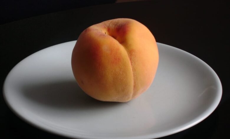 A single ripe peach rests on a white plate against a dark background.