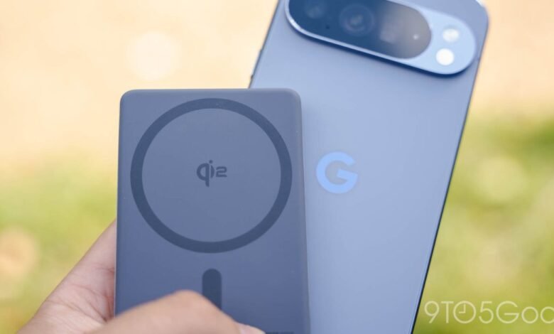A hand holds a dark gray Qi2 wireless charger next to a light blue Google Pixel phone.