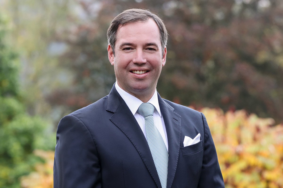 Portrait of Prince Guillaume of Luxembourg smiling, wearing a dark suit and light blue tie.