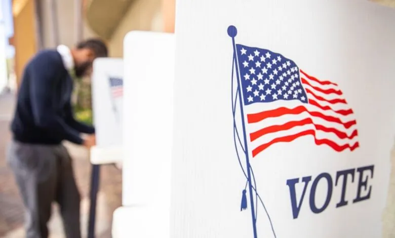 A person votes at a polling station with an American flag graphic and the word 'VOTE'.