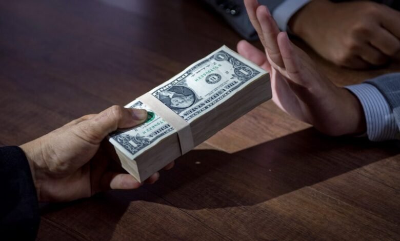A hand offers a stack of dollar bills, while another hand pushes them away.