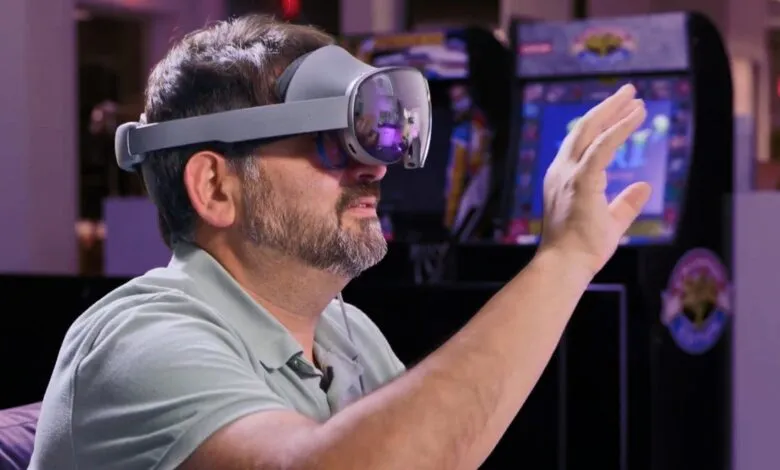 Man wearing a gray VR headset and reaching out his hand, with arcade games in the background.