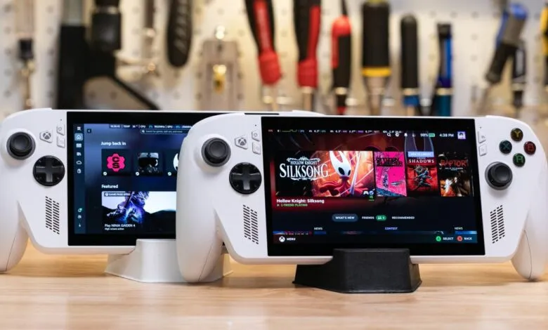 Two white handheld gaming PCs side-by-side on a wooden surface, displaying game libraries.