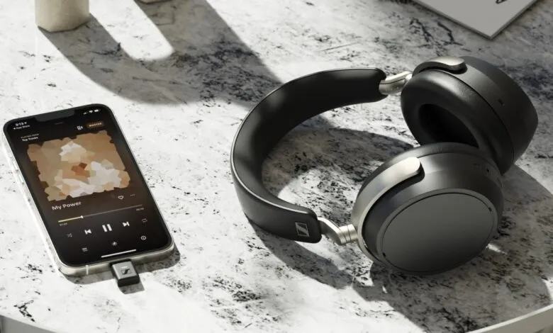 Black Sennheiser headphones and an iPhone playing music on a textured surface.